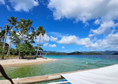 White sand beach with palm trees and turquoise water on an island hopping tour from DK2 Resort, El Nido.