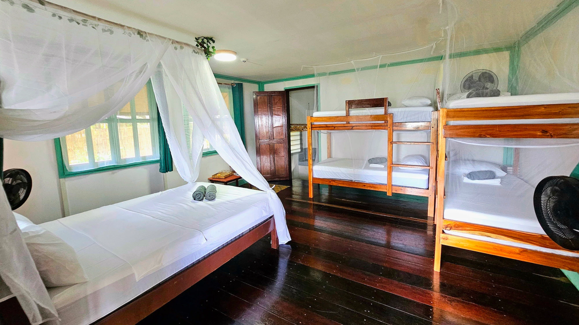 Spacious interior of the Palmscape Bungalow at DK2 Resort El Nido, featuring a queen bed with mosquito net and wooden bunk beds for families or groups.