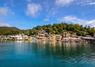Panoramic view of Liminangcong fishing village from the boat, featuring colorful stilt houses against a lush green hill.
